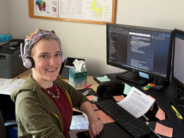 A light-skinned person wearing headphones sitting at a desk with a computer