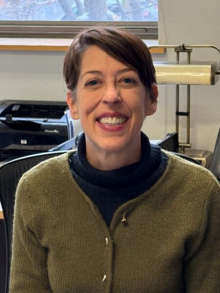 A light-skinned woman wearing a green sweater smiling for the camera