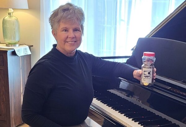 A light-skinned woman sitting at a piano holding a jar of coins