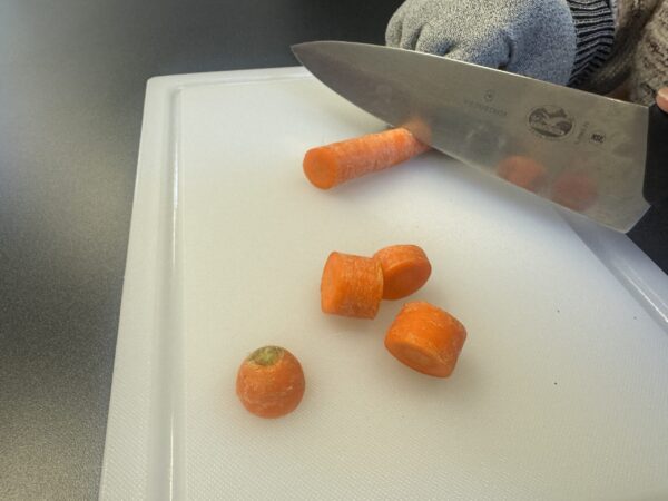 Two hands chopping a carrot with a knife on a cutting board.