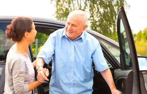 A woman helping a man out of a car