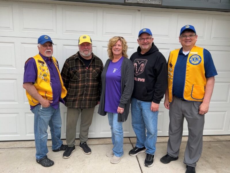 Five people wearing Lions Club caps and/or vests smiling for the camera