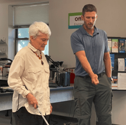 A light-skinned man instructing a light-skinned woman on using a white cane