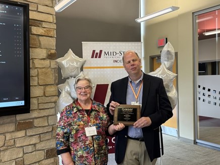 Jean Kalscheur and Jim Denham standing in a conference room holding a plaque.