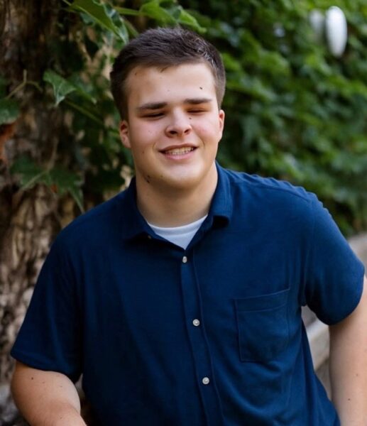 A light-skinned young man posing in front of some foliage