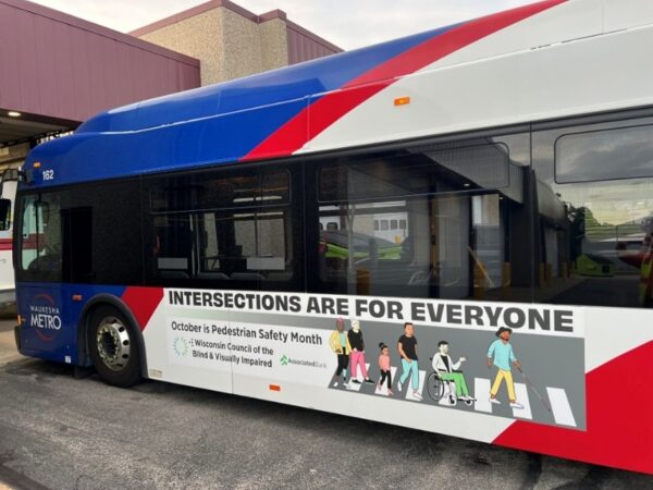 A Waukesha Metro bus with a large ad on the side reading Intersections are for Everyone along with the Council logo and a graphic of a diverse group of people crossing a street in a crosswalk.