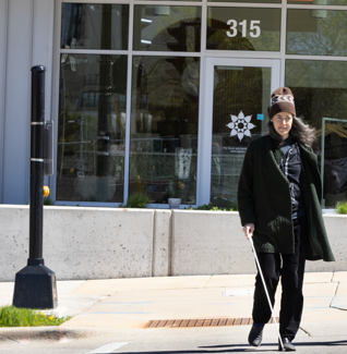 A person using a white cane crossing a street in a crosswalk