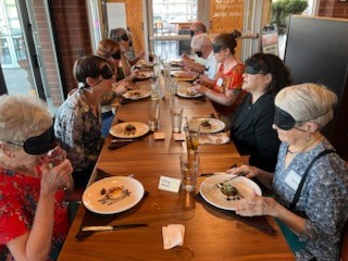 A group of blindfolded diners sitting at a long table.