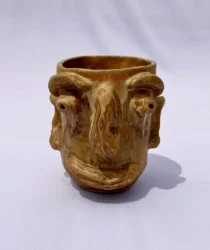 Gold-brown ceramic vessel with facial features on one side.