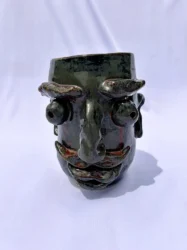 Ceramic vase with facial features including thick mustache and eyebrows.