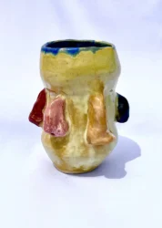 Yellow vase with blue around the rim and different color noses protruding from the sides.