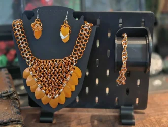 A matched set of earrings, a bracelet and necklace made out of orange and silver rings and scales