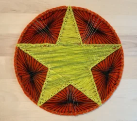 A 3D piece featuring a five-pointed textile gold star on circular patterned backing mounted on wood.