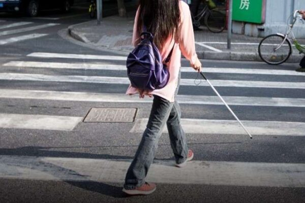 A person with a white cane walking in a crosswalk